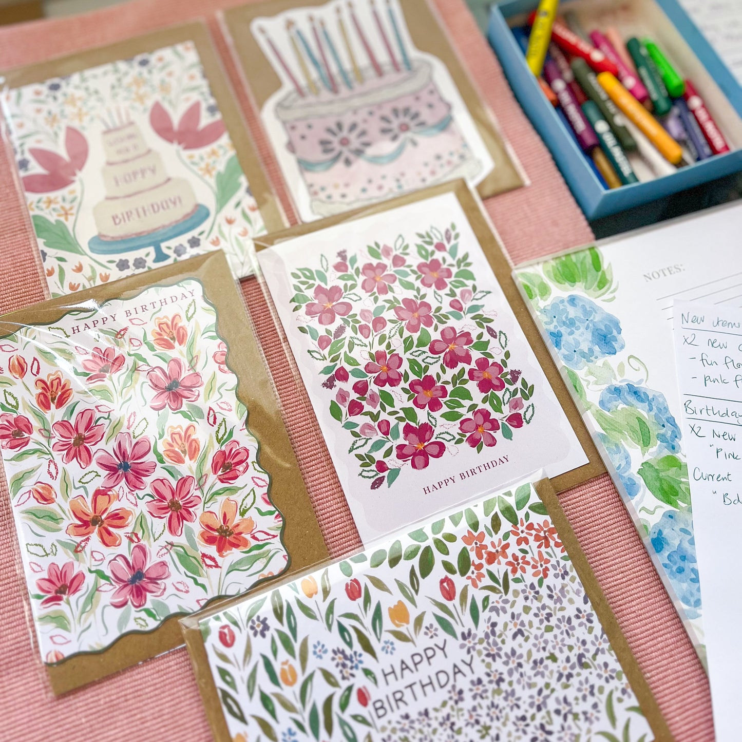 Collection of handmade birthday cards with floral and cake designs on a pink surface.