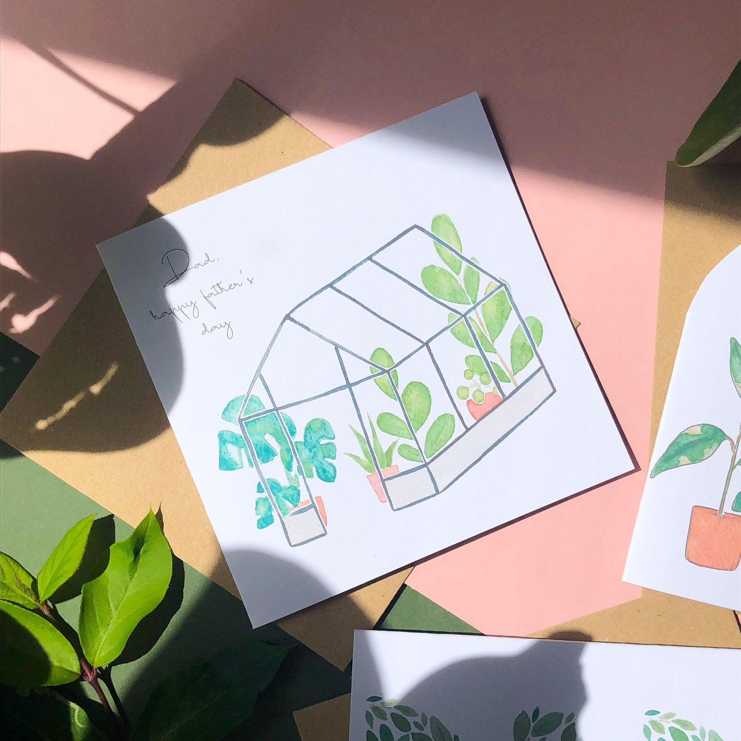 A square Father's Day card with a beautifully painted image of a tropical greenhouse, teeming with lush foliage and exotic blooms. The card also features the words "Dad Happy Father's Day" in an elegant cursive font, written in a contrasting colourful tone to the background painting. This card is a thoughtful and striking way to honour a special dad on his day, with the vibrant colours and intricate details of the painting adding to its unique appeal.