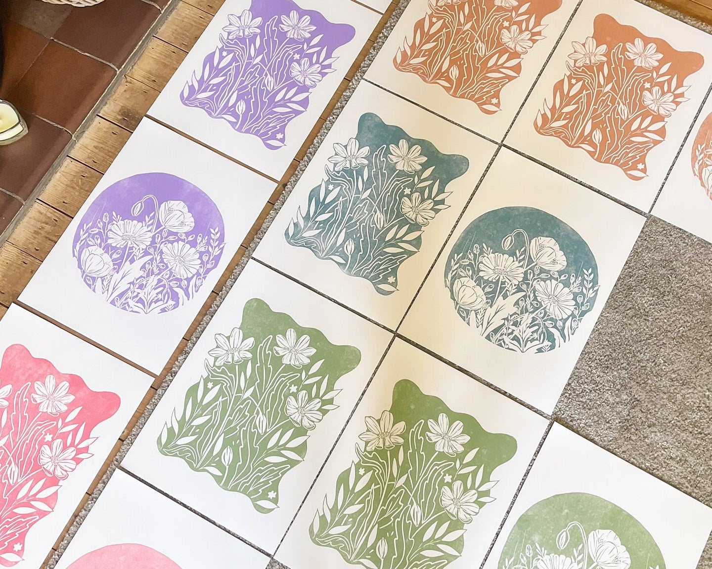 Colorful floral designs on white paper laid out on a wooden floor.