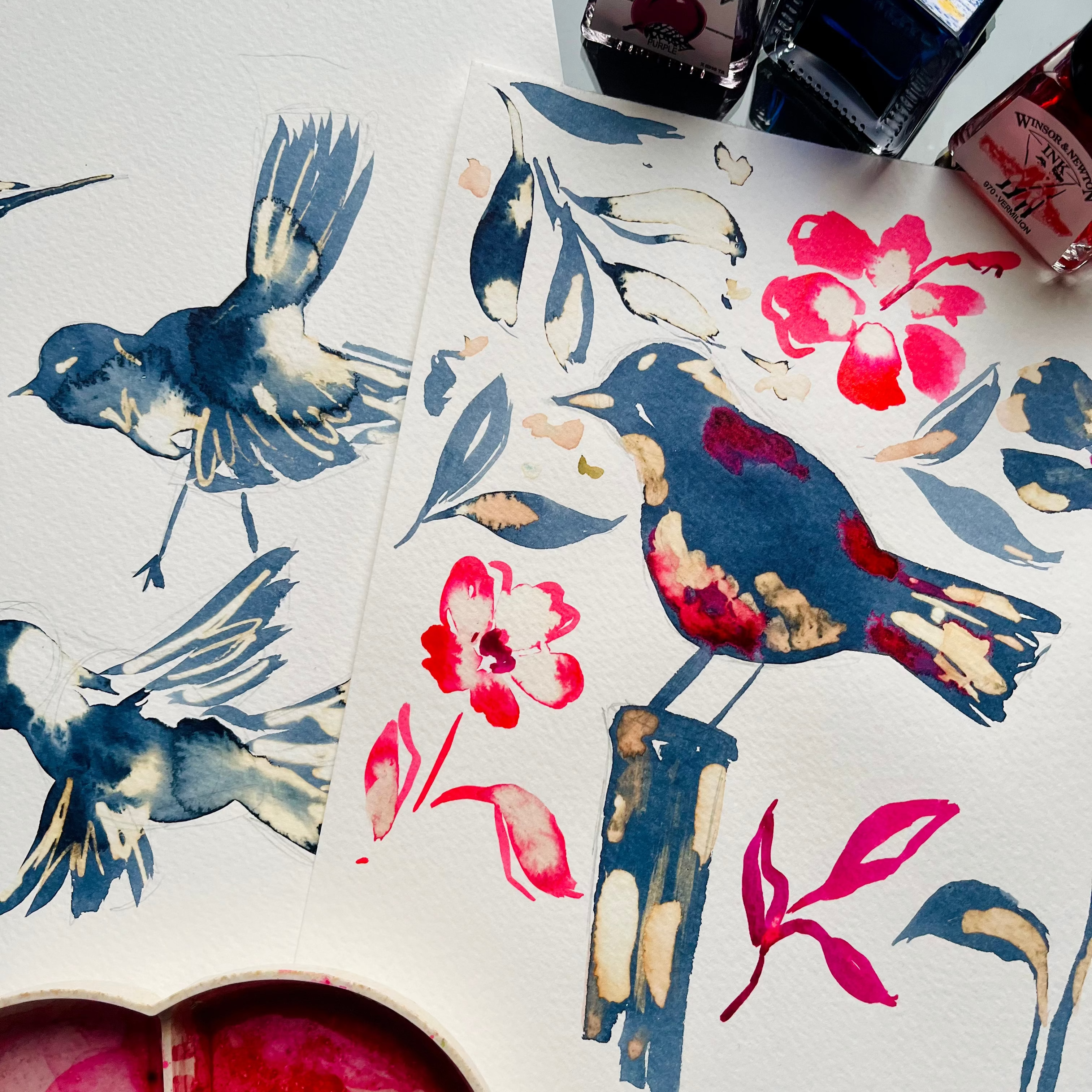 Artistic watercolor illustrations of birds and flowers on a white surface with ink bottles.