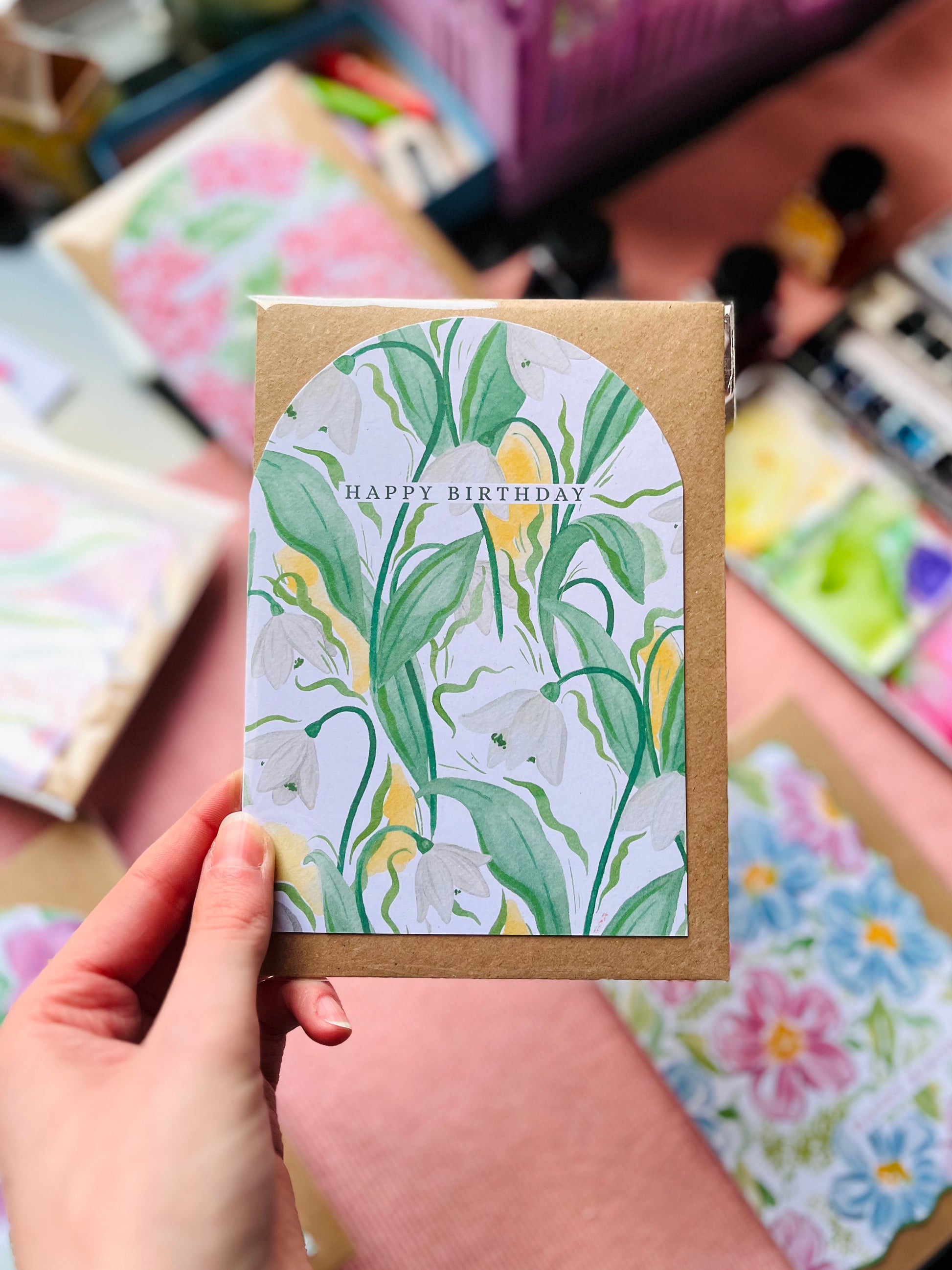 Hand holding a floral birthday card with watercolor designs in the background