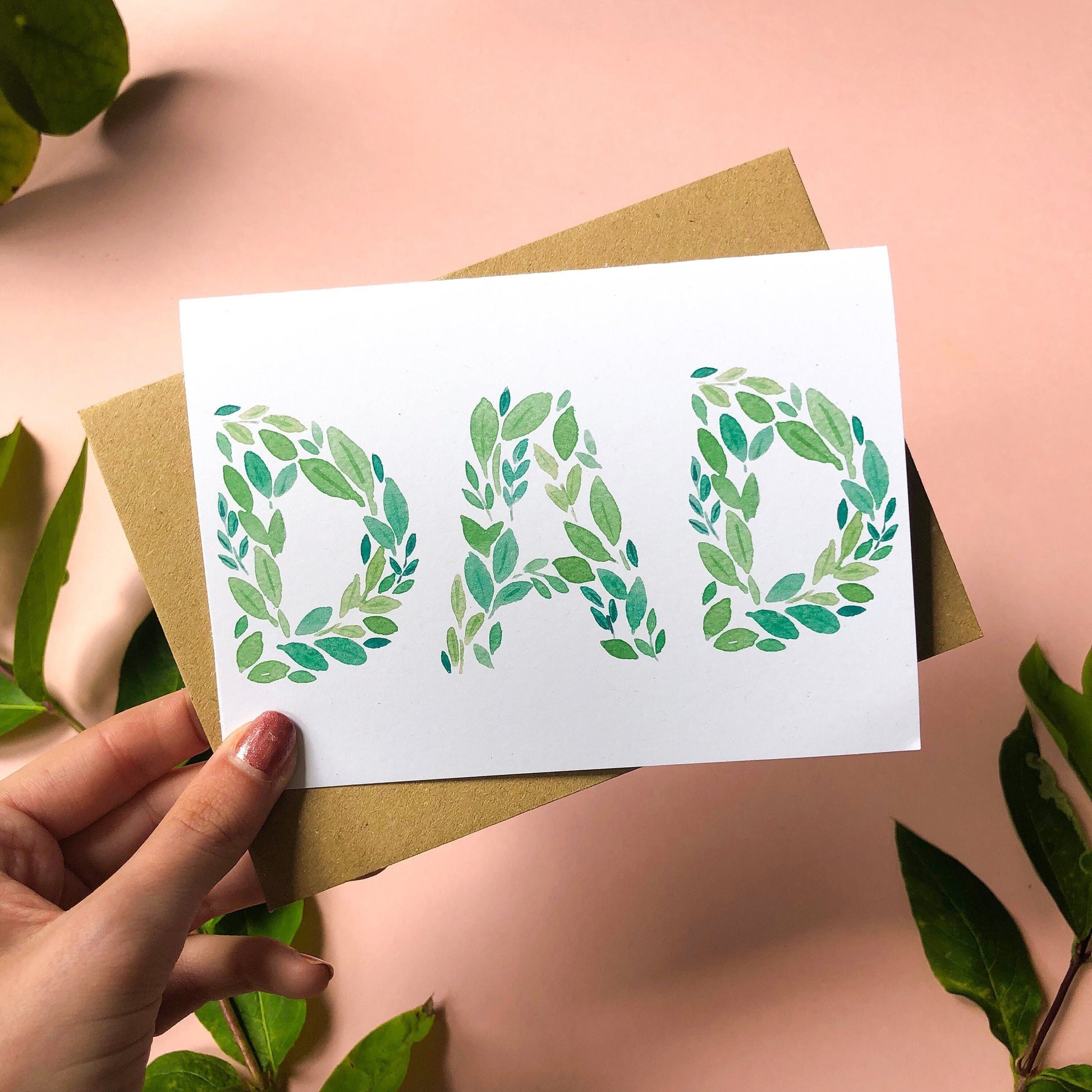 A Father's Day card with the word "DAD" spelled out beautifully in green leaves of various shades and shapes. The card offers a simple yet elegant way to show appreciation and affection for a beloved dad on his special day.
