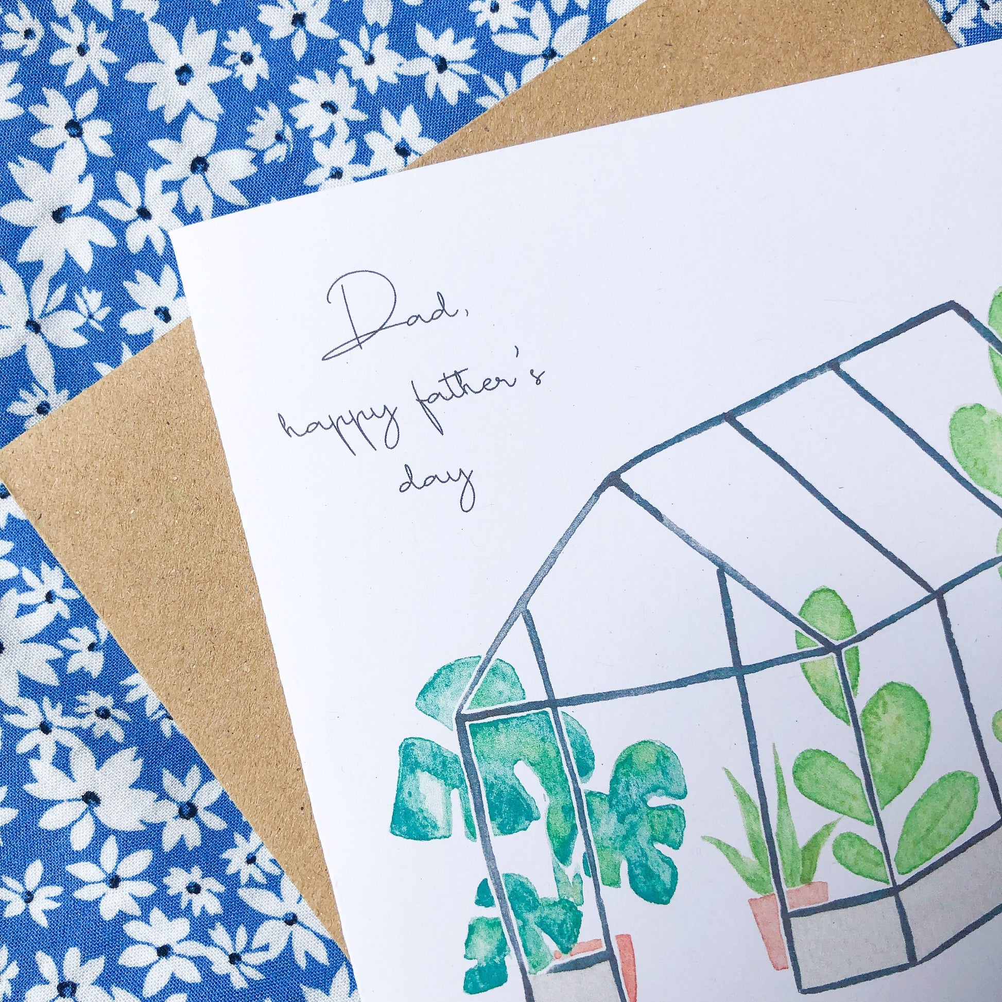 A square Father's Day card with a beautifully painted image of a tropical greenhouse, teeming with lush foliage and exotic blooms. The card also features the words "Dad Happy Father's Day" in an elegant cursive font, written in a contrasting colourful tone to the background painting. This card is a thoughtful and striking way to honour a special dad on his day, with the vibrant colours and intricate details of the painting adding to its unique appeal.